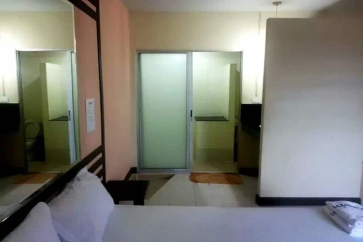 A hotel room with a bed, a mirror, a sliding door to the bathroom, and a small rug on the floor.