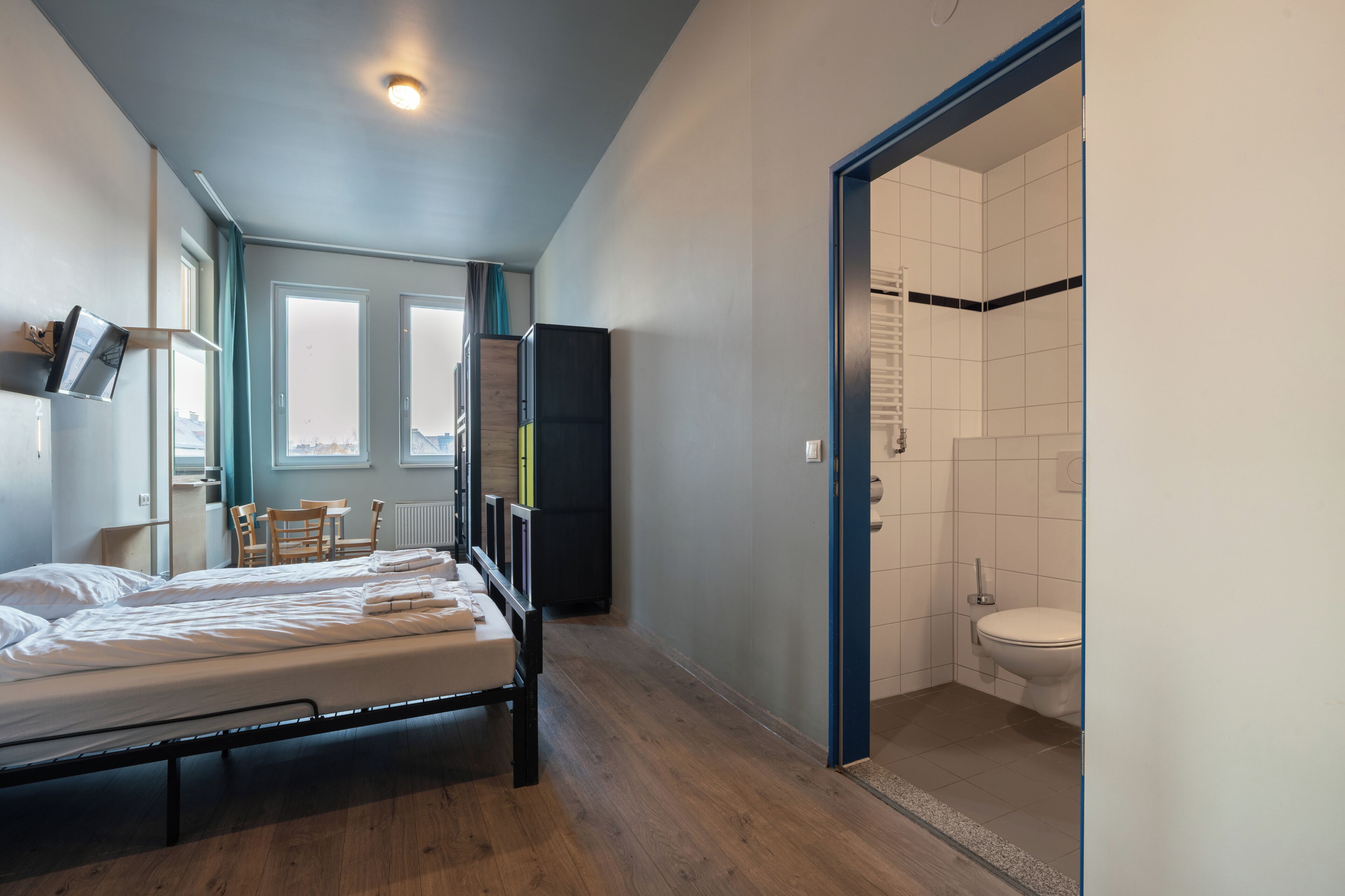 Une chambre d’hôtel comprenant un lit, un bureau, une chaise, une armoire et une salle de bain avec des toilettes et une douche.