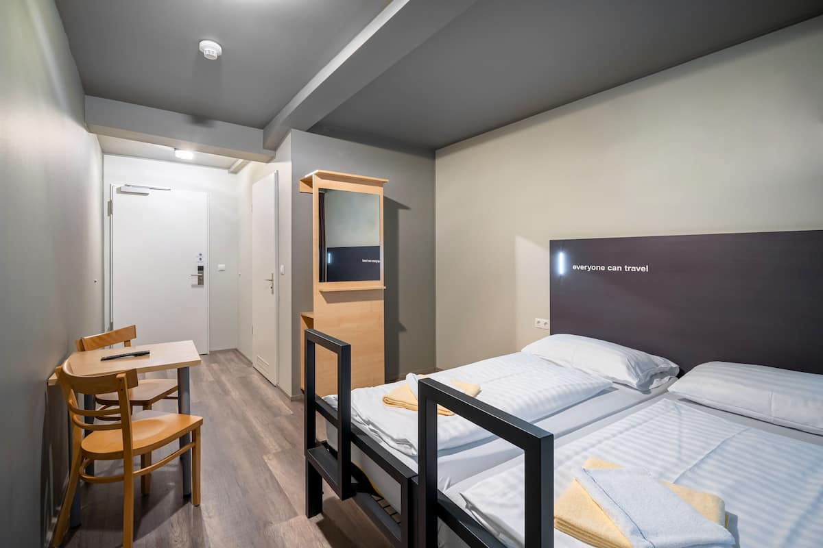 Et moderne hotelværelse med køjeseng, skrivebord med stol, spejl og vægmonteret tv.