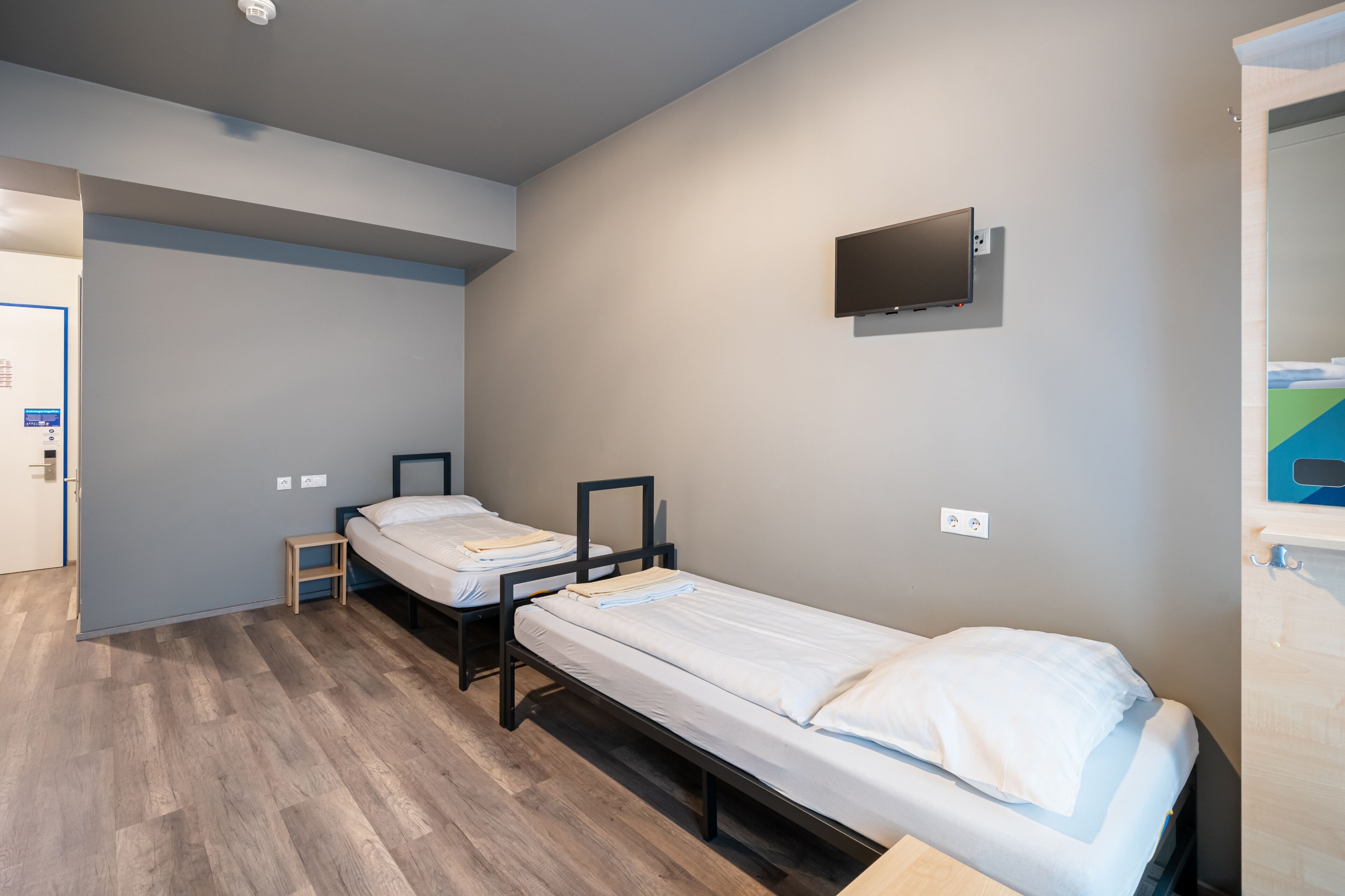 Une chambre dotée de deux lits simples, d’un téléviseur à écran plat fixé au mur et d’un plancher en bois.