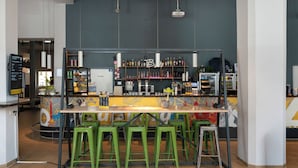 A bar area with stools, shelves of bottles, and a neon sign. - a&o Hostel Salzburg Hauptbahnhof (Salzburg)