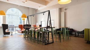 A modern interior with a swing set, green and orange chairs, and a large window. - a&o Hostel Salzburg Hauptbahnhof (Salzburg)
