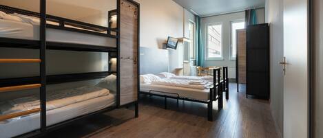 A bunk bed room with a desk, a chair, a TV, and a wardrobe.
