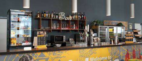 A bar area with a 'Welcome to' sign, shelves with bottles, a refrigerator, and stools.