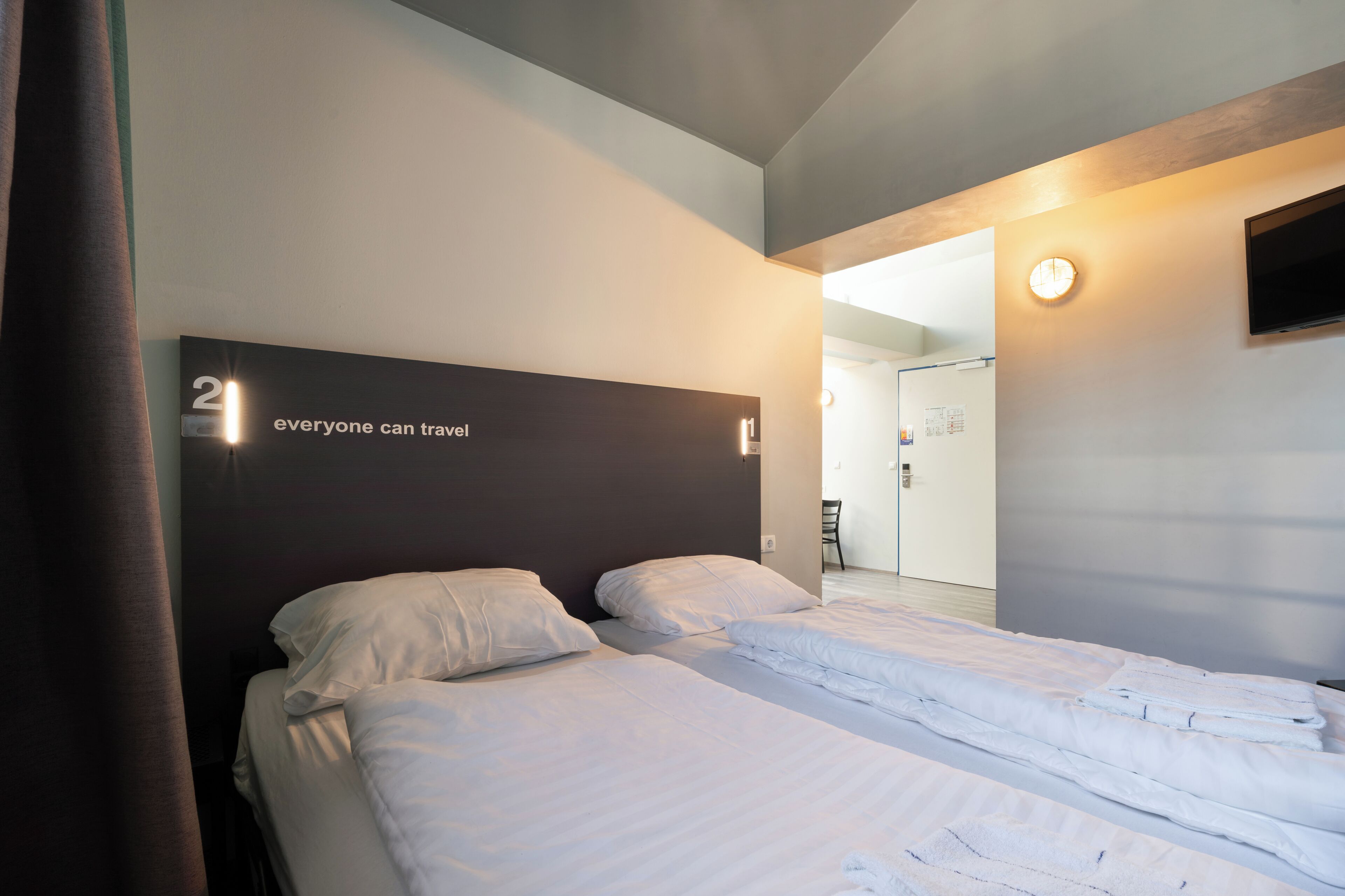 A hotel room with two beds, a flat-screen TV, and a door leading to a bathroom.