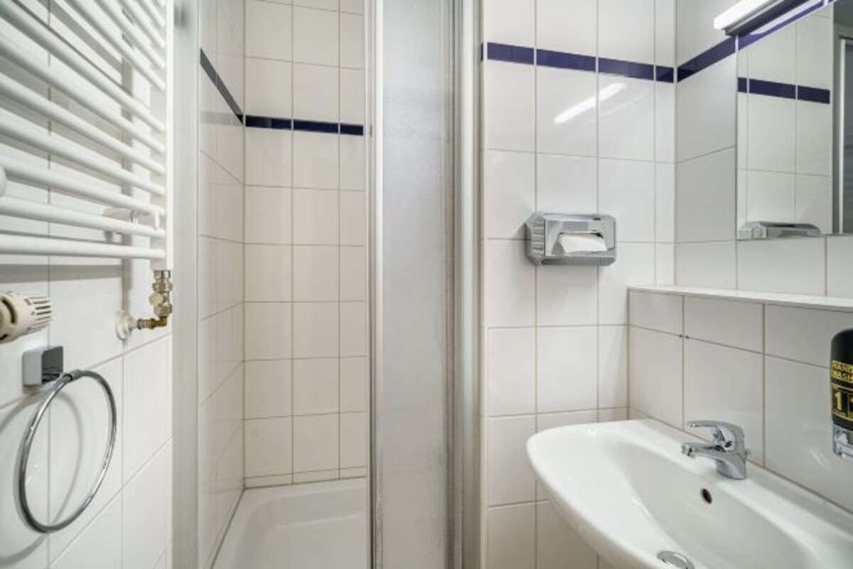 Un bagno con doccia, lavandino, porta asciugamani e specchio.