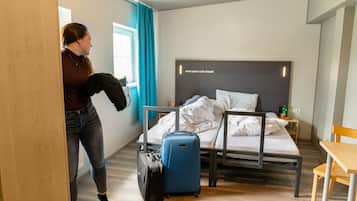 A hotel room with a bed, a desk, and a suitcase.
