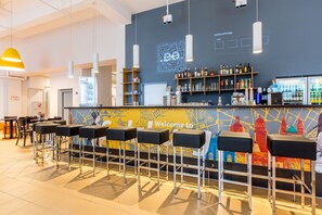 A bar area with stools, a counter with a QR code, shelves with bottles, and a colorful mural. - a&o Salzburg Hauptbahnhof - Hostel (Salzburg)