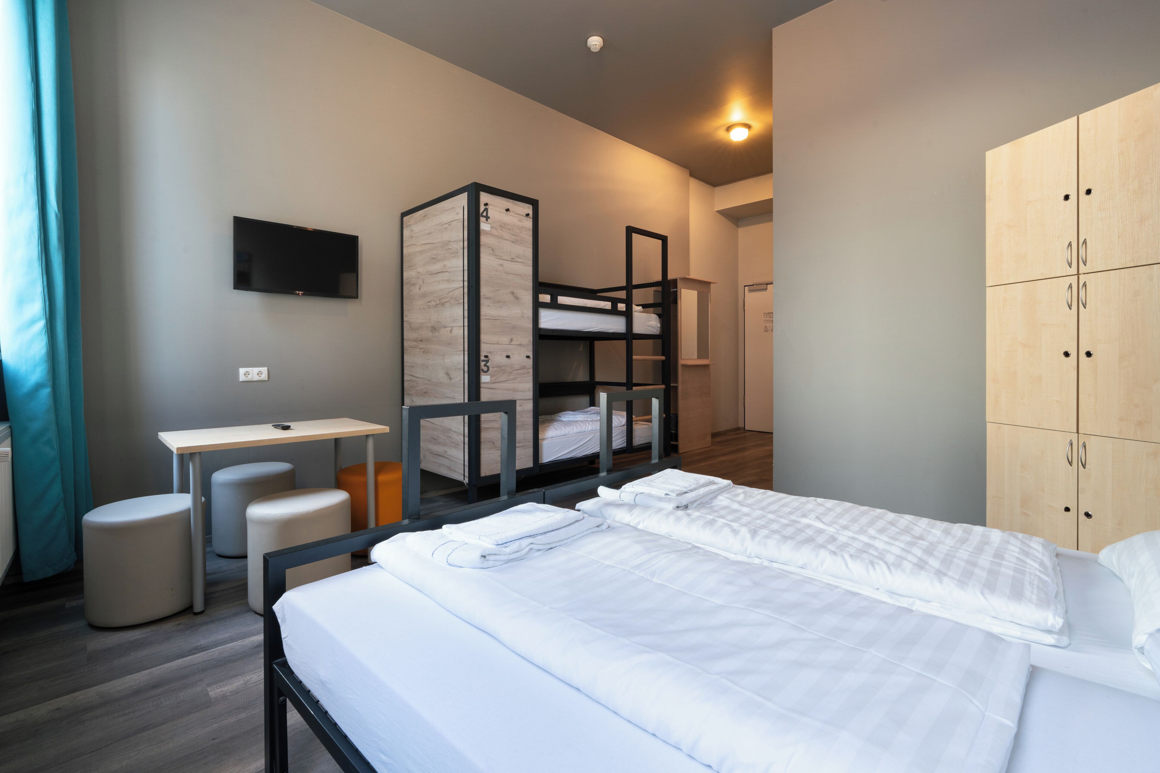 A hotel room with a bunk bed, a desk, a chair, a TV, and a wardrobe.
