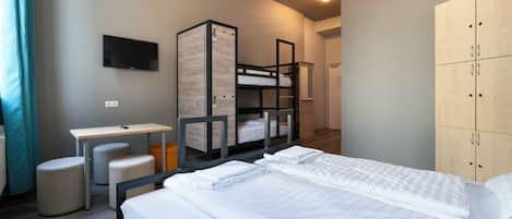 A hotel room with a bunk bed, a desk, a chair, a TV, and a wardrobe.