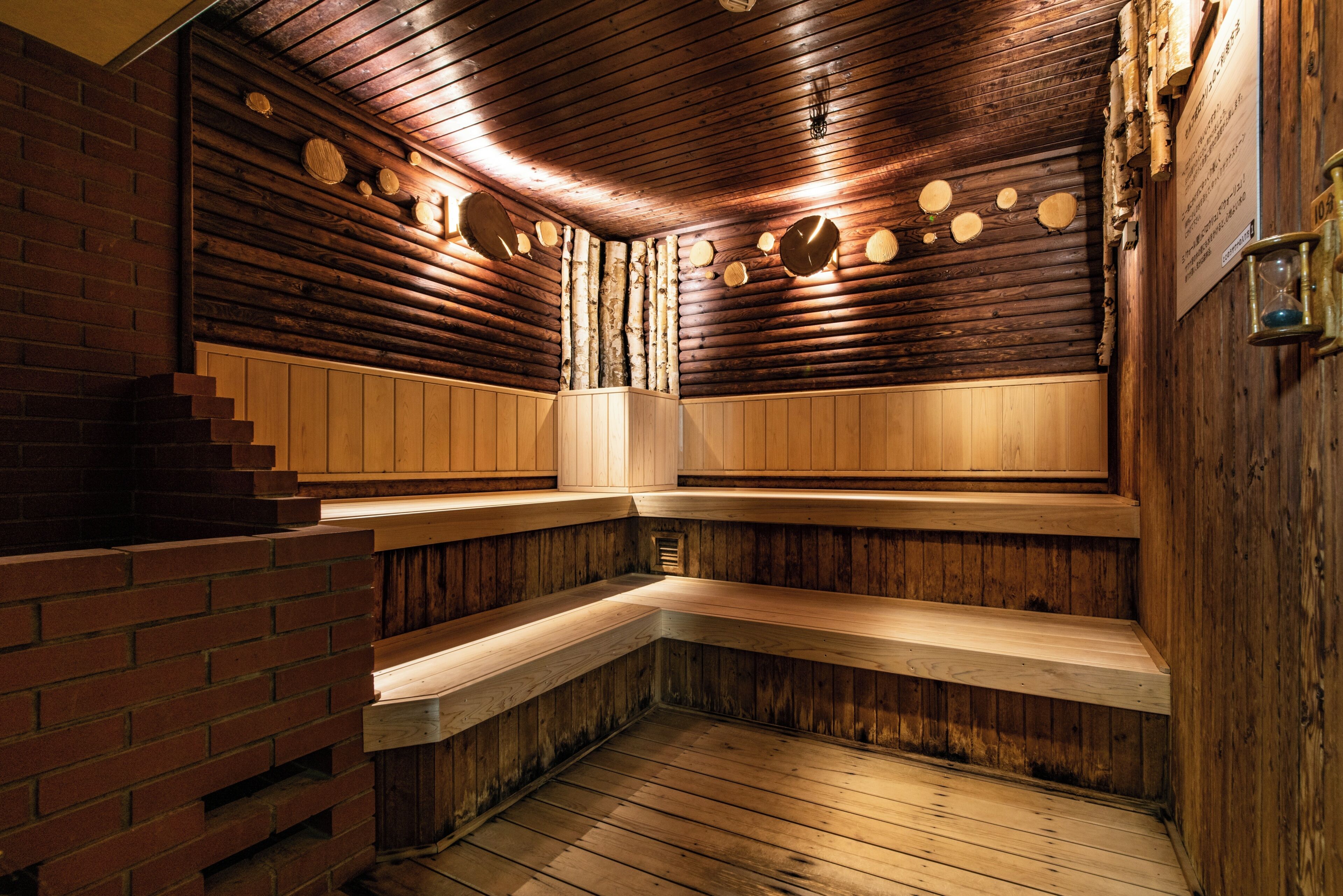 A sauna with wooden walls and benches, a brick wall on one side, and a wooden floor.