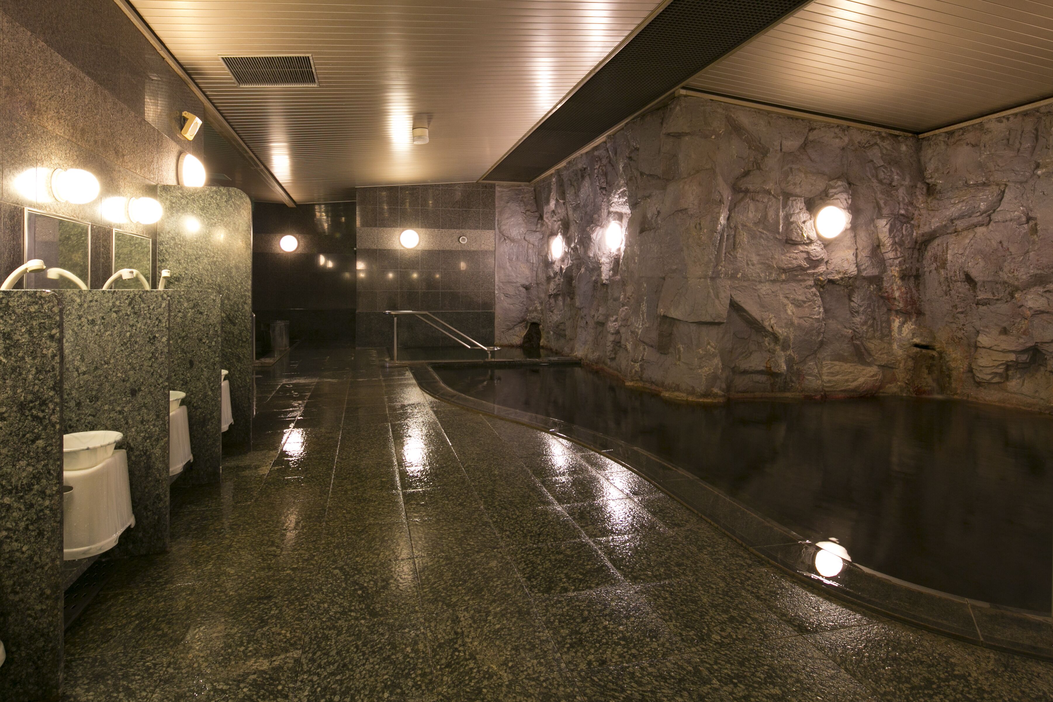 A modern indoor pool with a wet floor, stone walls, and multiple lights.