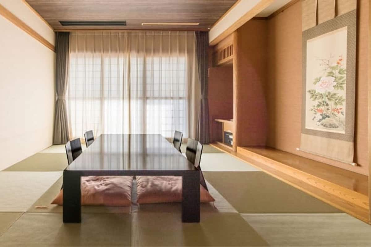 A traditional Japanese tatami room with a low table and chairs, a shoji screen, and a painting on the wall.