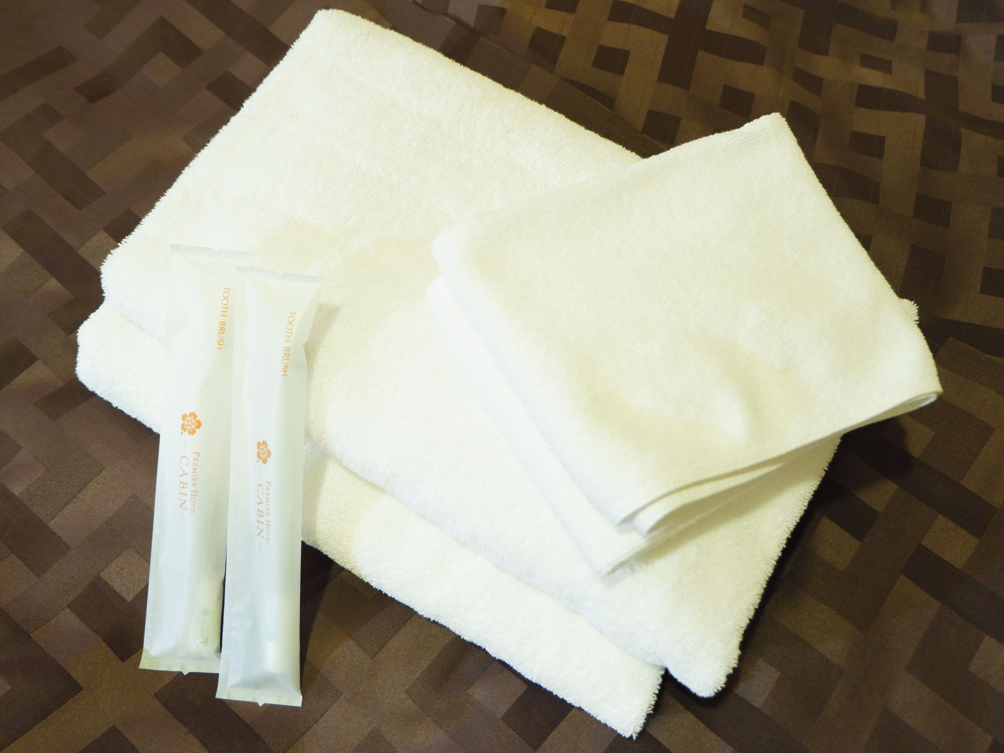 A white towel and a tube of toothpaste on a patterned surface.