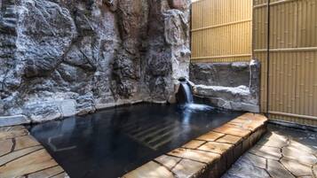 A hot spring area with a stone pool, a waterfall, and a bamboo fence.