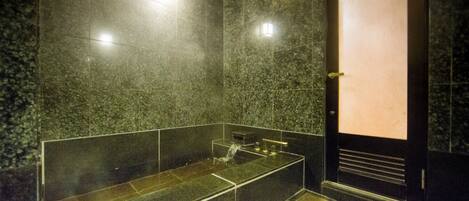 A modern bathroom with a glass-enclosed shower, dark marble walls, and a door with a light panel.