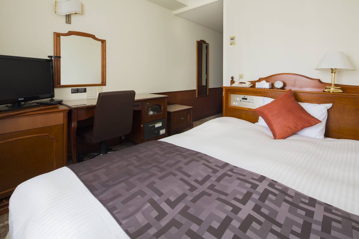 A hotel room with a bed, a desk with a computer, a television, and a mirror.