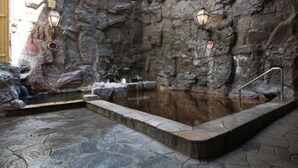 A spa area with a hot tub, stone walls, and two wall-mounted lights. - Premier Hotel Cabin Obihiro (Obihiro)