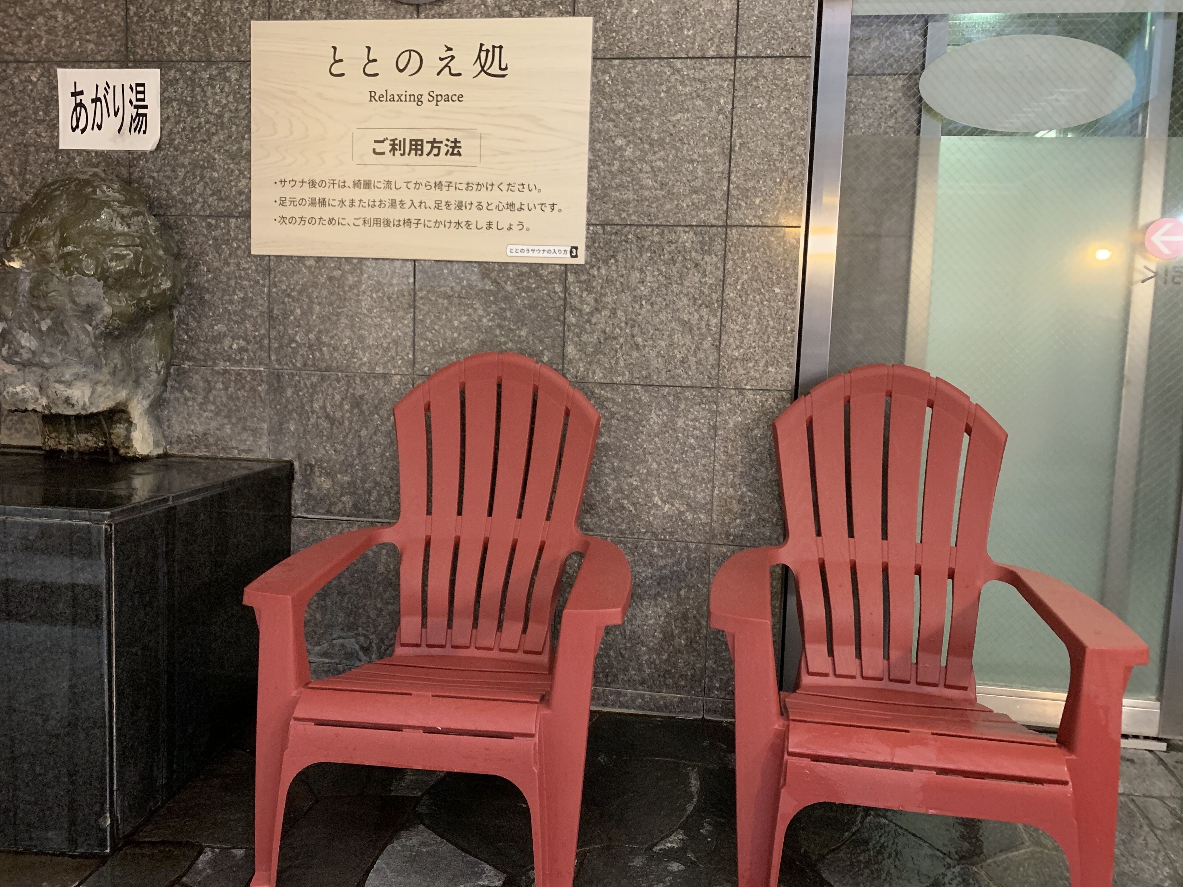 Dos sillas rojas en un área de recepción con una pared de piedra y un cartel.