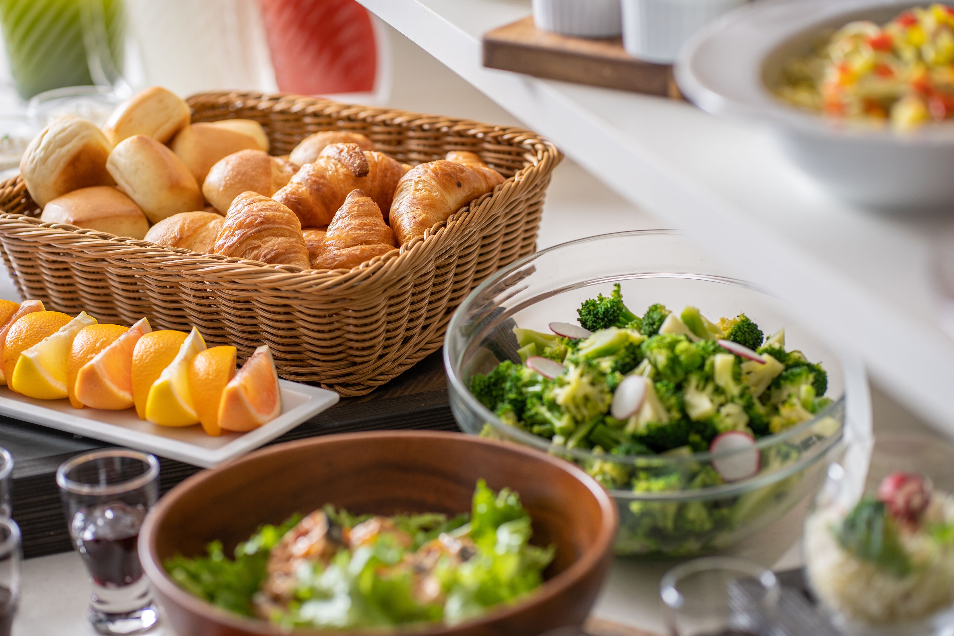 A breakfast buffet with croissants, orange slices, and various salads.