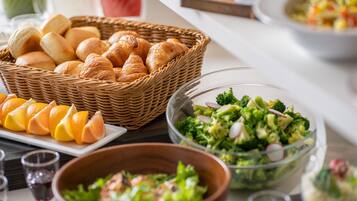A breakfast buffet with croissants, orange slices, and various salads.