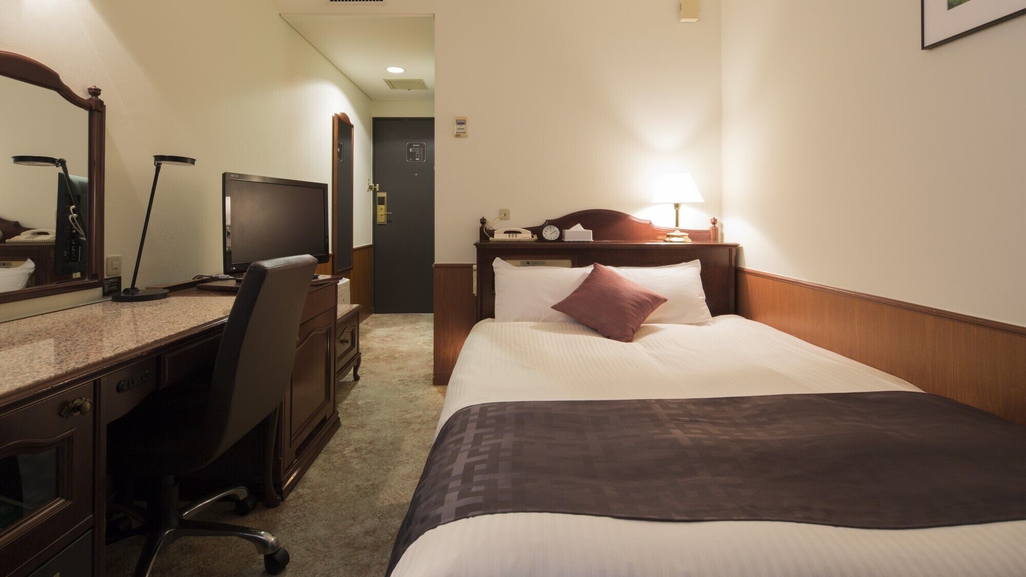 A hotel room with a bed, desk, chair, and a television.