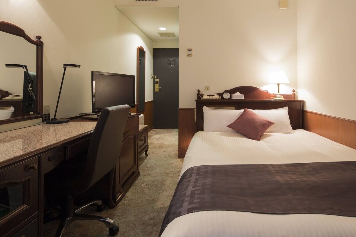A hotel room with a bed, desk, chair, and a television.