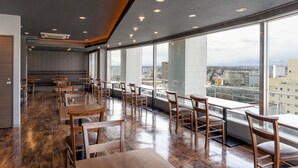 A modern restaurant with wooden tables and chairs, large windows offering city views, and recessed ceiling lighting. - Premier Hotel Cabin Obihiro (Obihiro)