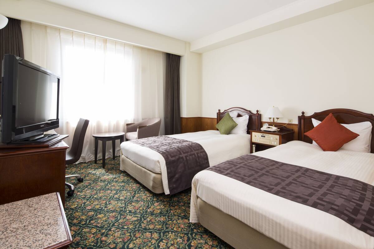 A hotel room with two beds, a television, a desk, and a chair.