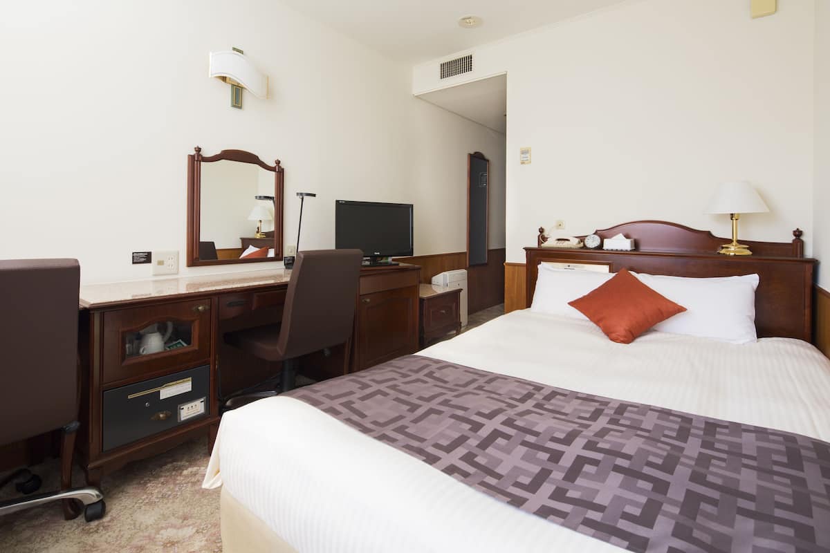A hotel room with a bed, desk, chair, and a television.