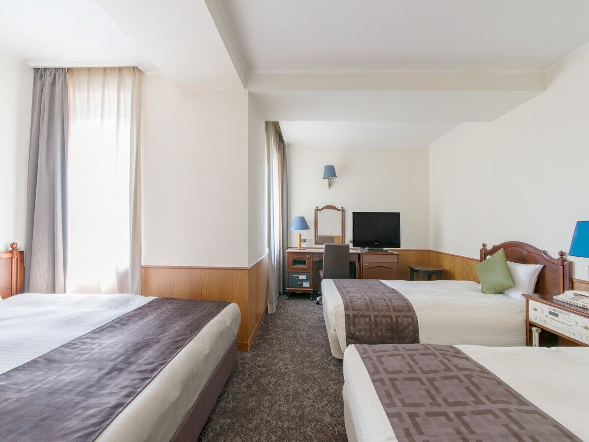 A hotel room with two beds, a desk, a television, and a lamp.