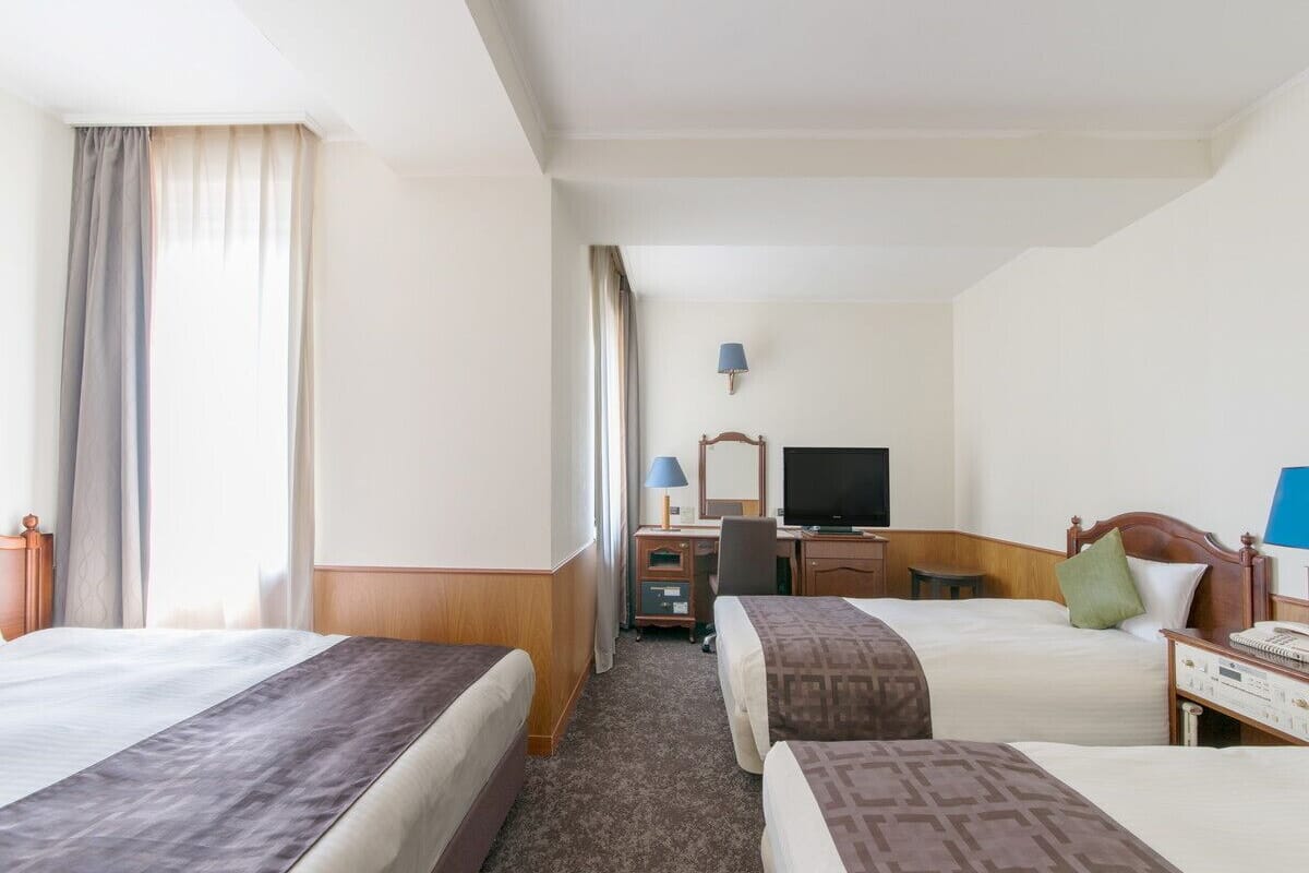 A hotel room with two beds, a desk, a television, and a lamp.