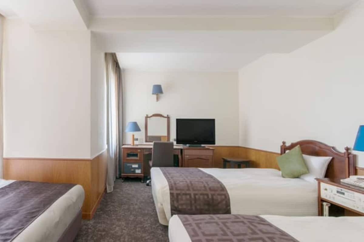 A hotel room with two beds, a desk with a computer, a TV, and a lamp.