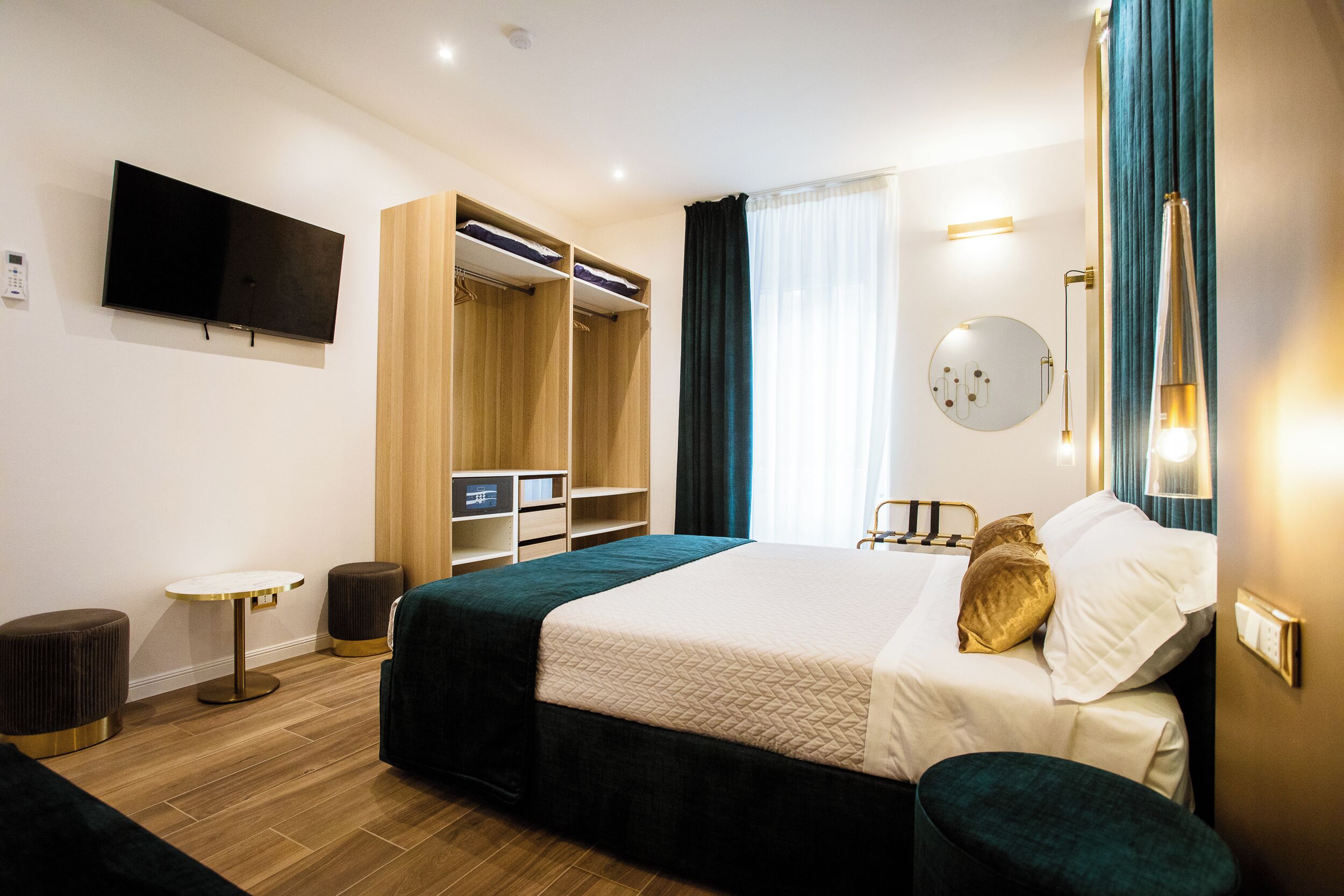 A modern hotel room with a large bed, a TV mounted on the wall, a wardrobe, and a bedside table.