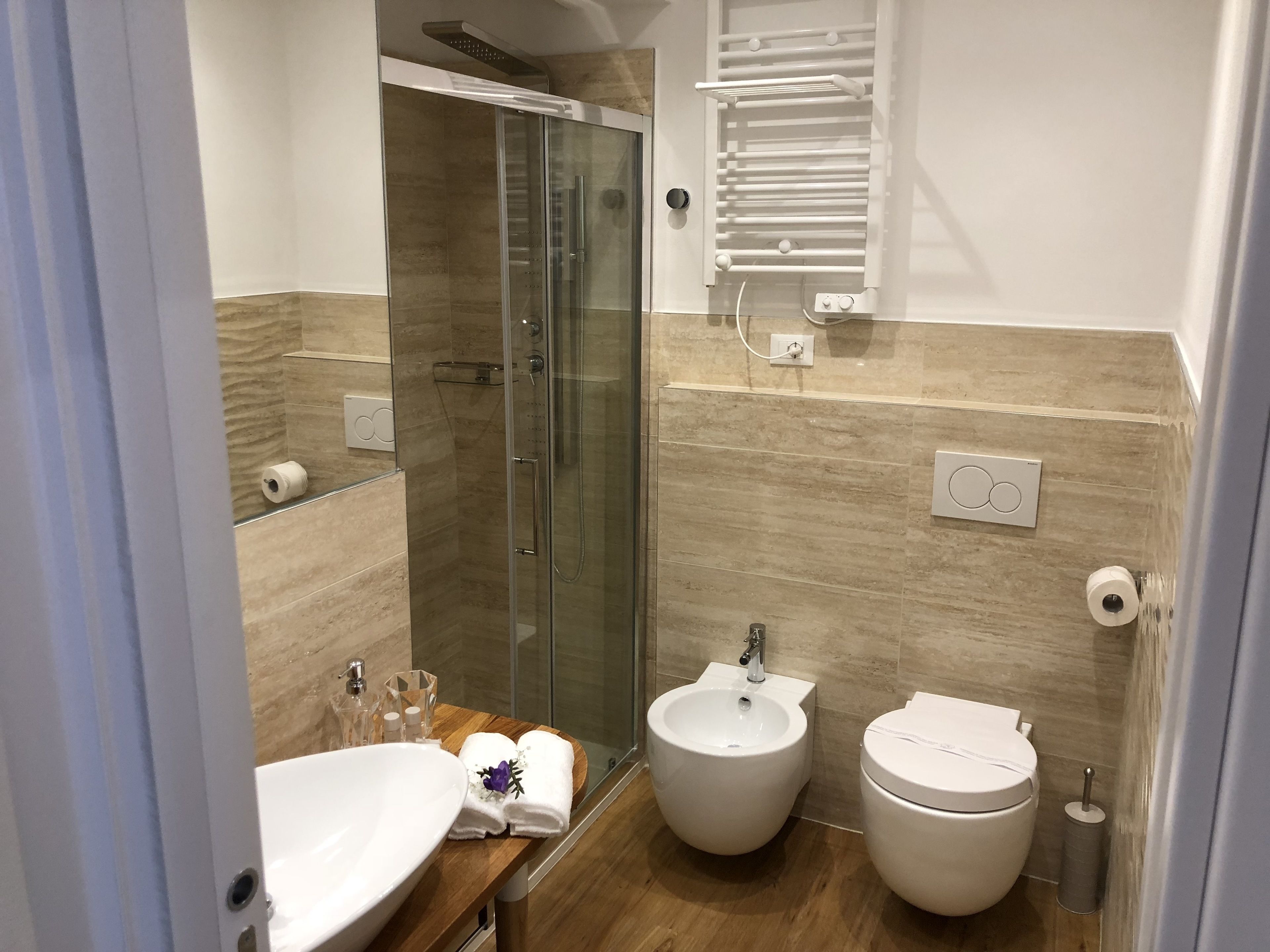 A modern bathroom with a glass-enclosed shower, a bidet, a toilet, and a sink with toiletries.