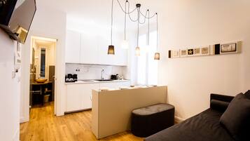 Un espacio habitable pequeño con kitchenette, un sofá y un pequeño otoman.