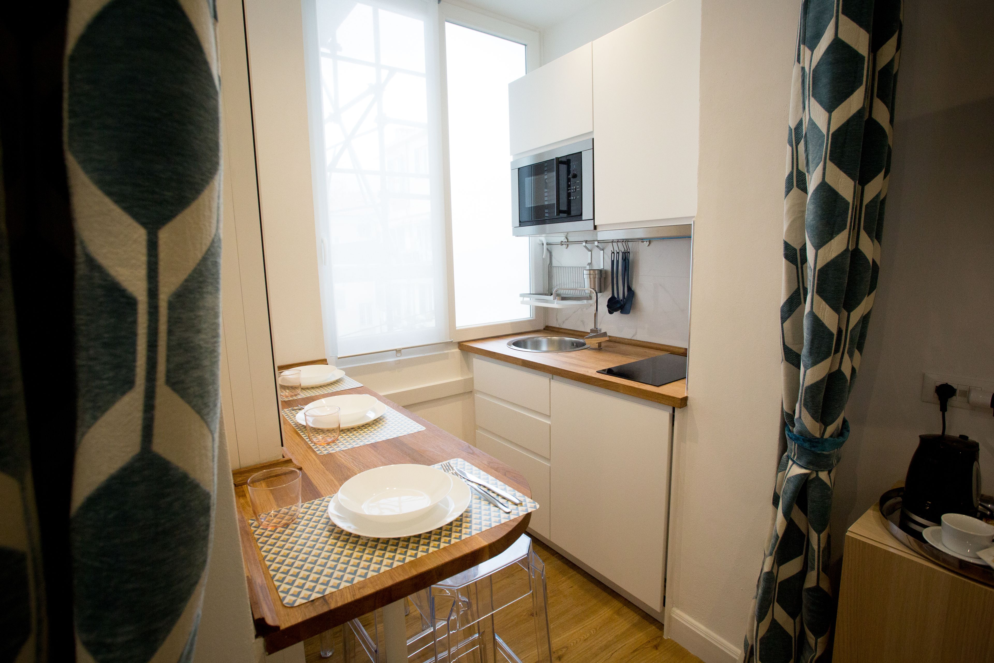 A compact kitchen with a microwave, sink, and wooden countertop.