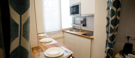 Una cocina compacta con microondas, pileta y encimera de madera.