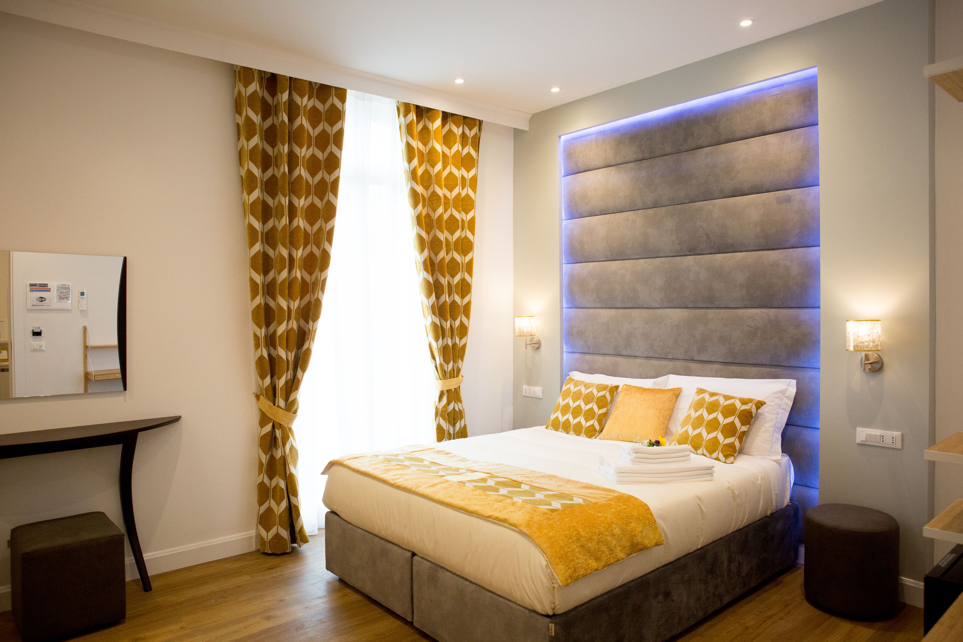 Una habitación de hotel moderna con una cama grande, un escritorio y un cabecero con iluminación integrada.