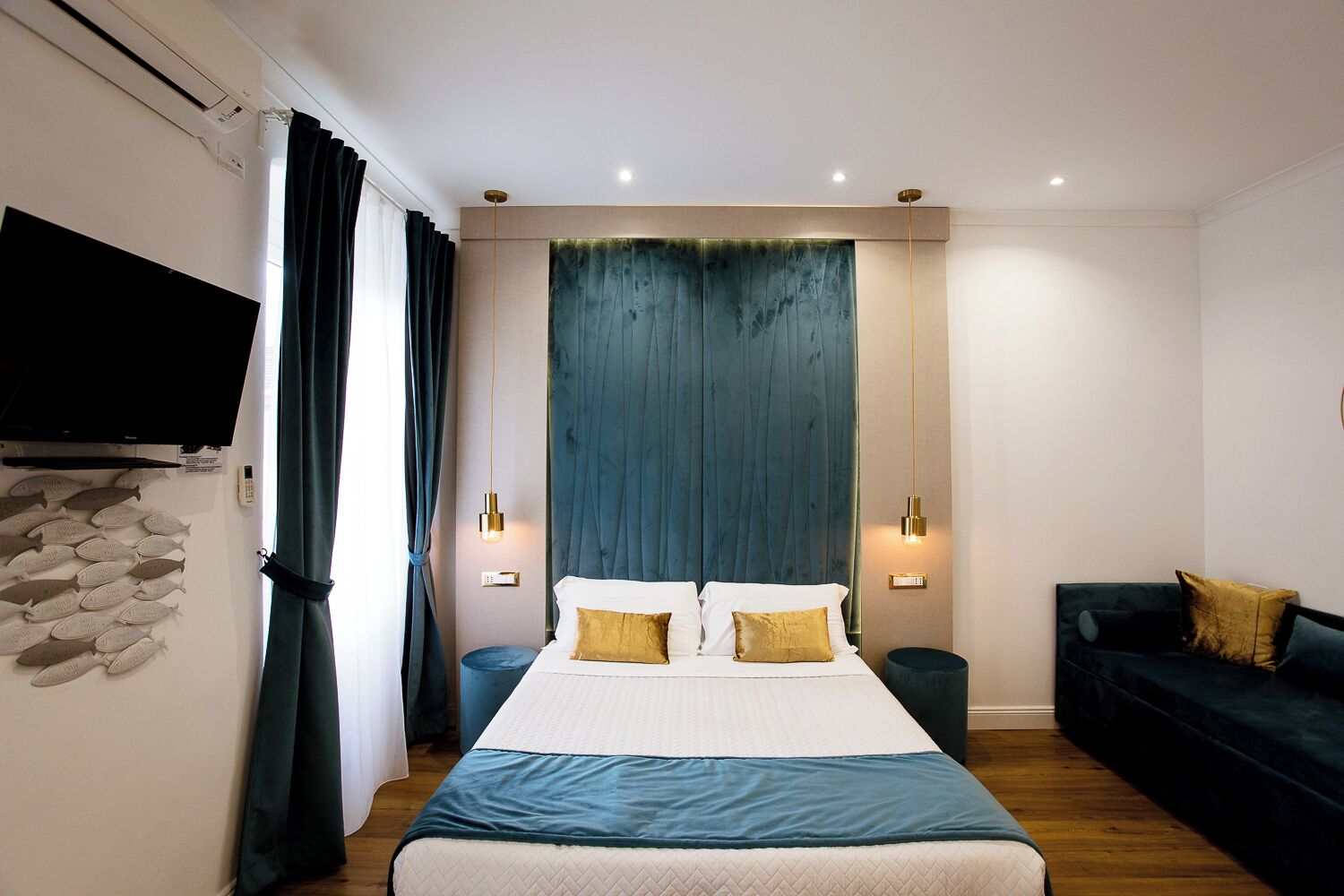 Ein modernes Schlafzimmer mit einem großen Bett, zwei Nachttischen, einem dunklen Sofa und einem an der Wand montierten Fernseher.