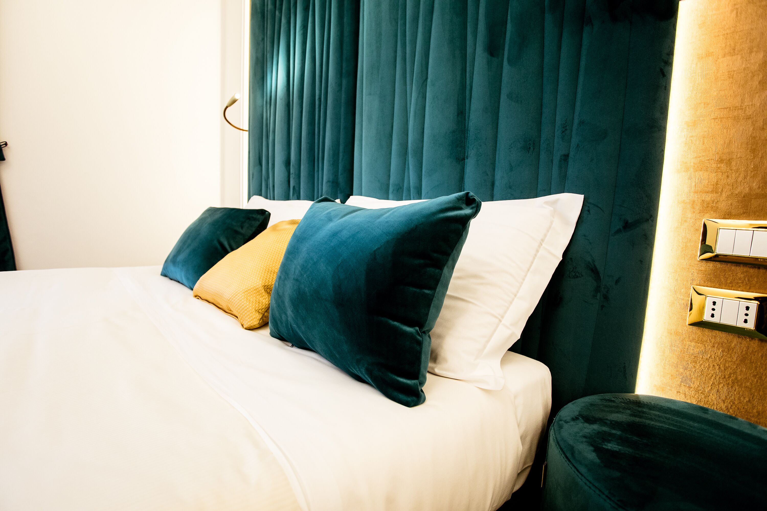 Una cama con ropa de cama blanca y verde azulada, un cojín amarillo y cojines verde azulada.