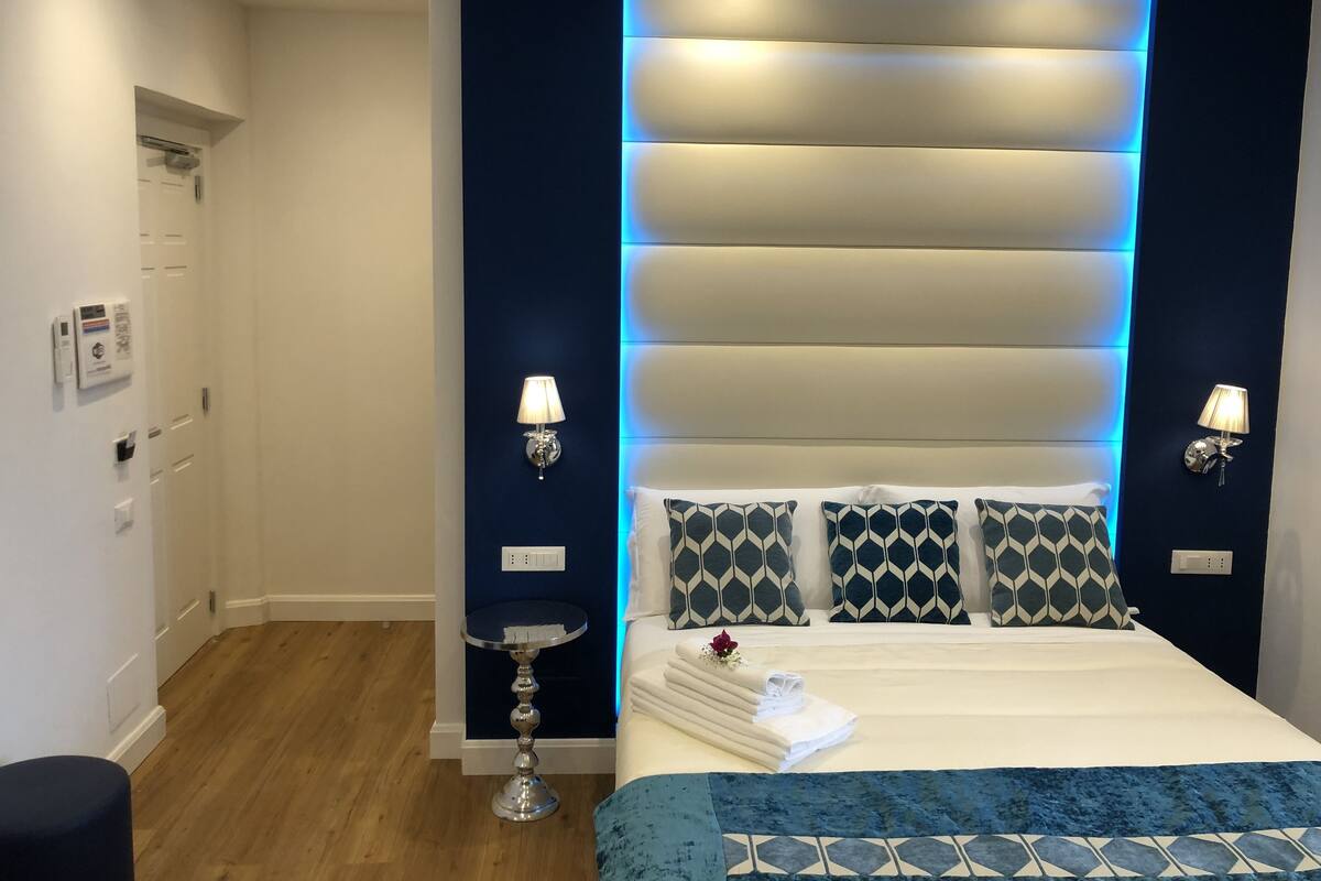 Ein modernes Hotelzimmer mit Bett, Nachttischlampen, einem kleinen runden Tisch und einer Wandleuchte.