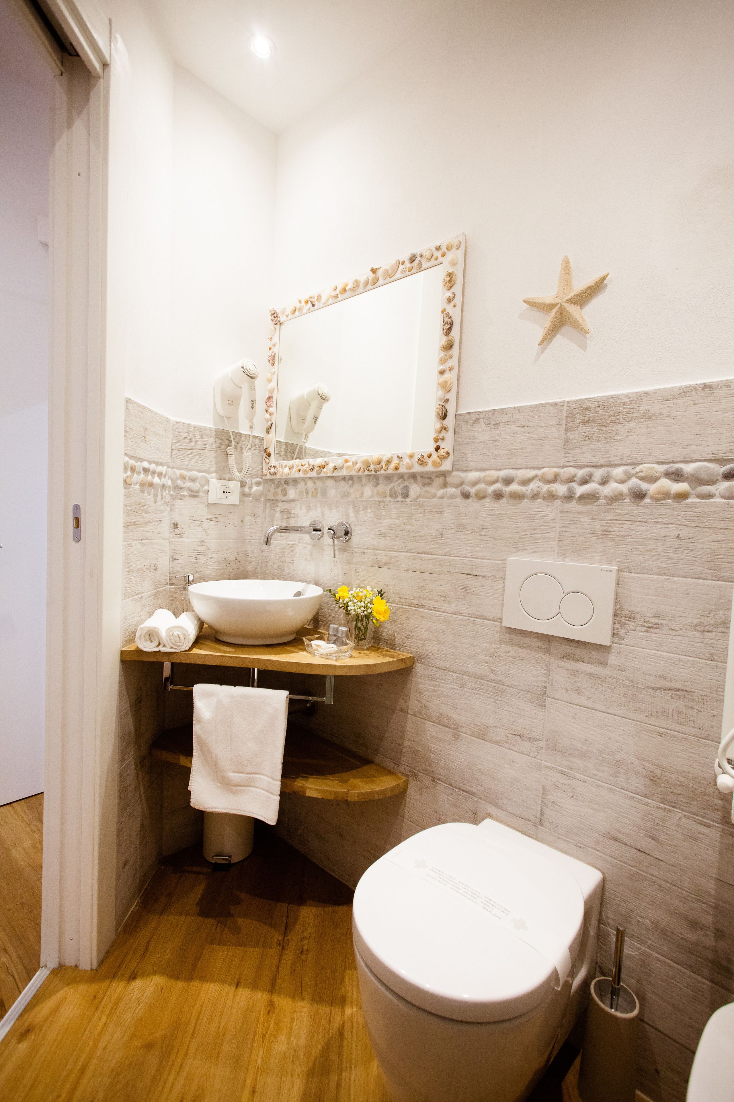 A bathroom with a wooden vanity, a white sink, a mirror with a seashell frame, a toilet, and a starfish decoration on the wall.