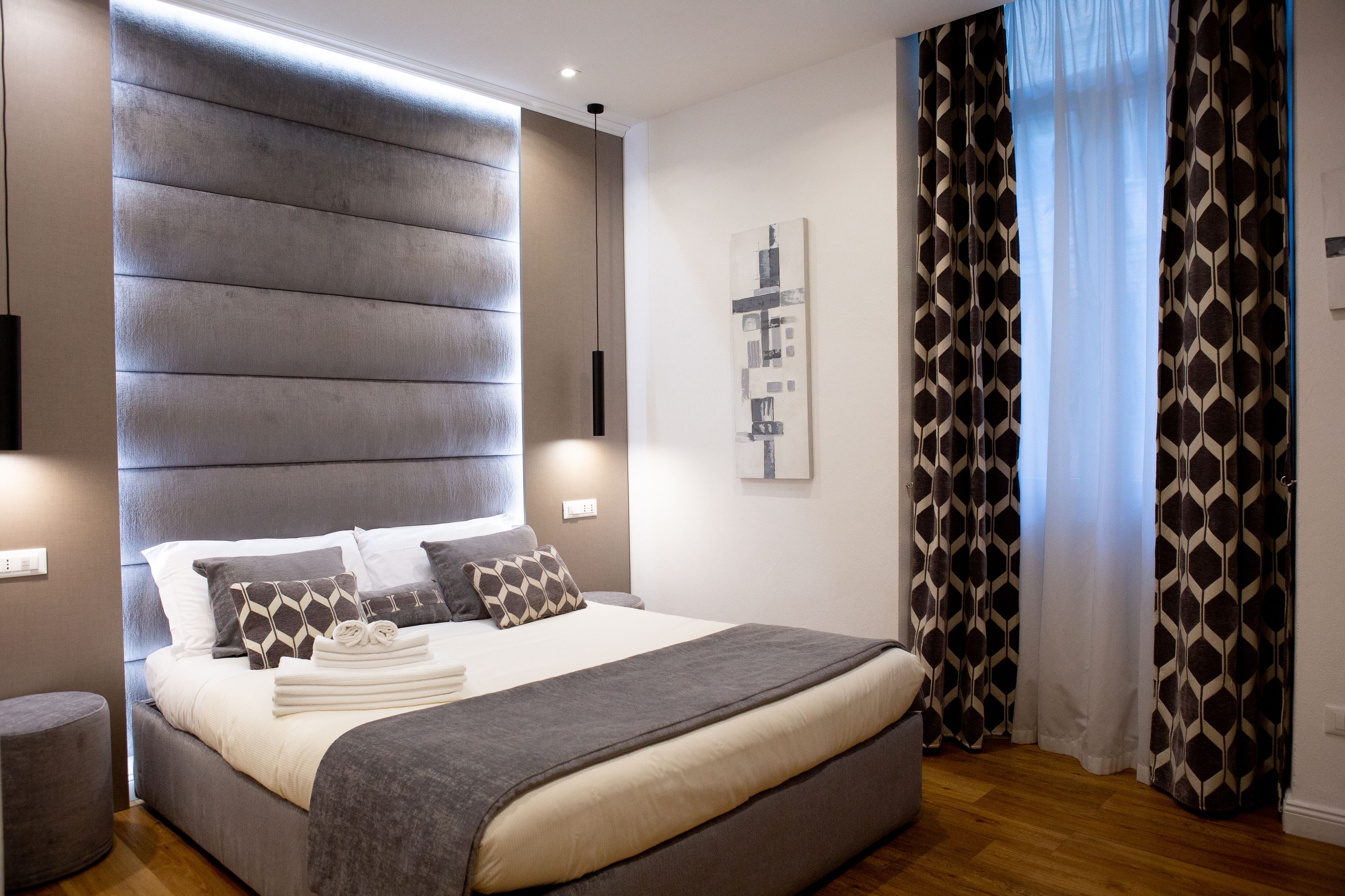A modern bedroom with a large bed, a headboard, bedside tables, and a wall-mounted artwork.