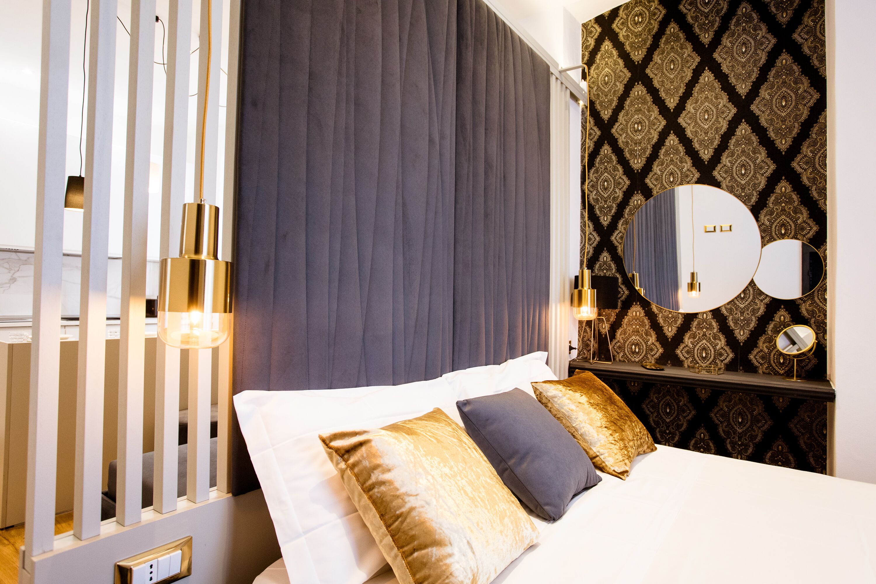 A modern hotel room with a bed, a large mirror, and a patterned wallpaper.