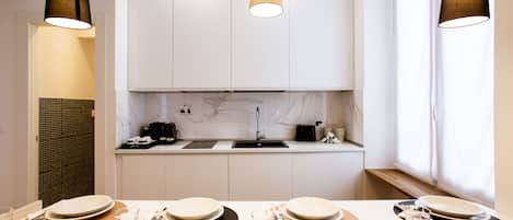 A modern kitchen with white cabinets, a marble backsplash, and pendant lighting.