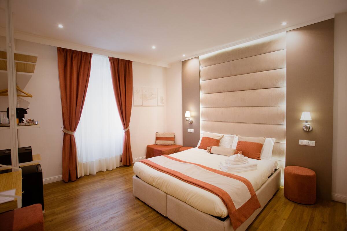 Ein modernes Schlafzimmer mit einem großen Bett, Nachttischen, einem Kleiderschrank und einem Fenster mit Vorhängen.