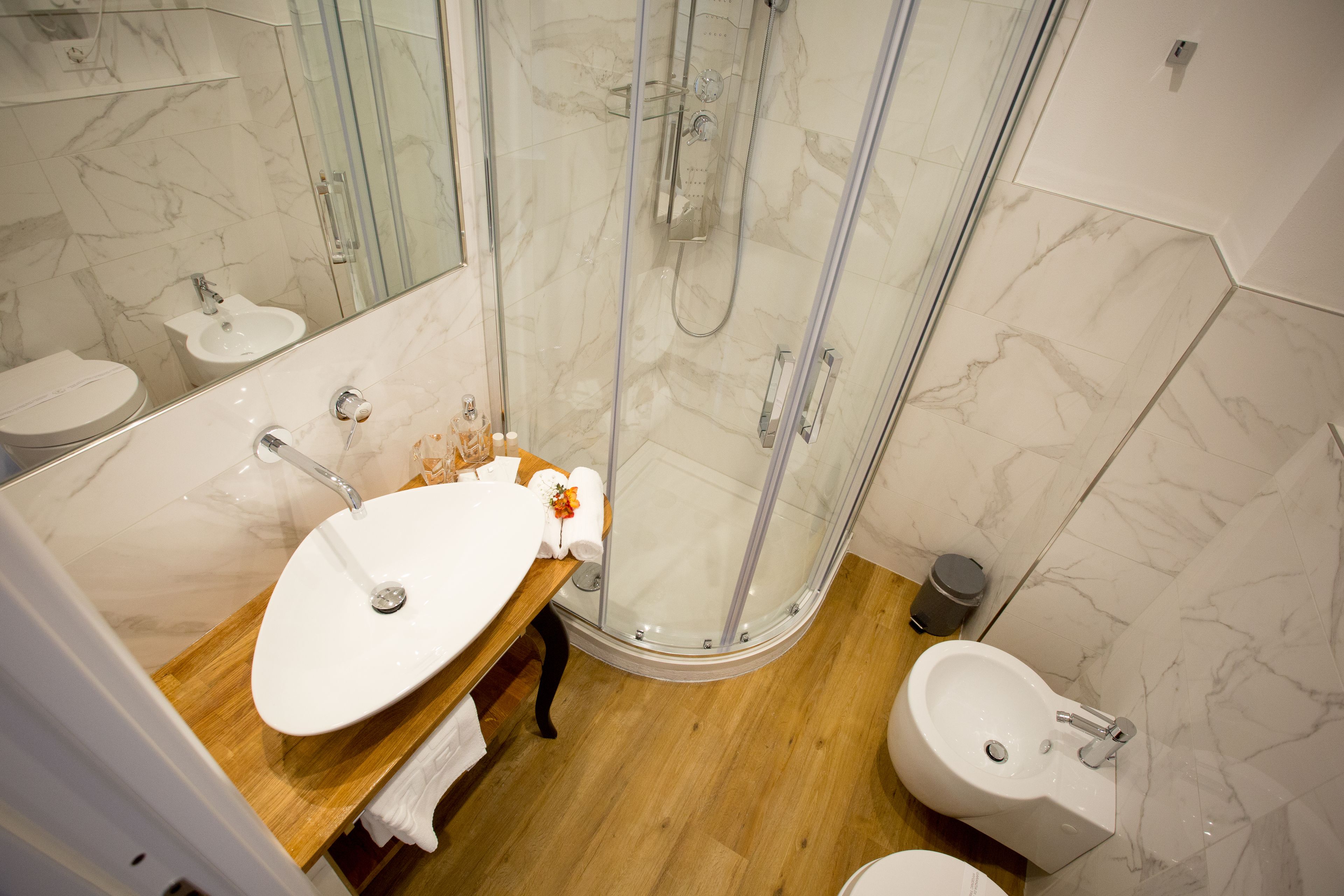 Un baño moderno con ducha envuelta en vidrio, tocador de madera y dos lavamanos.
