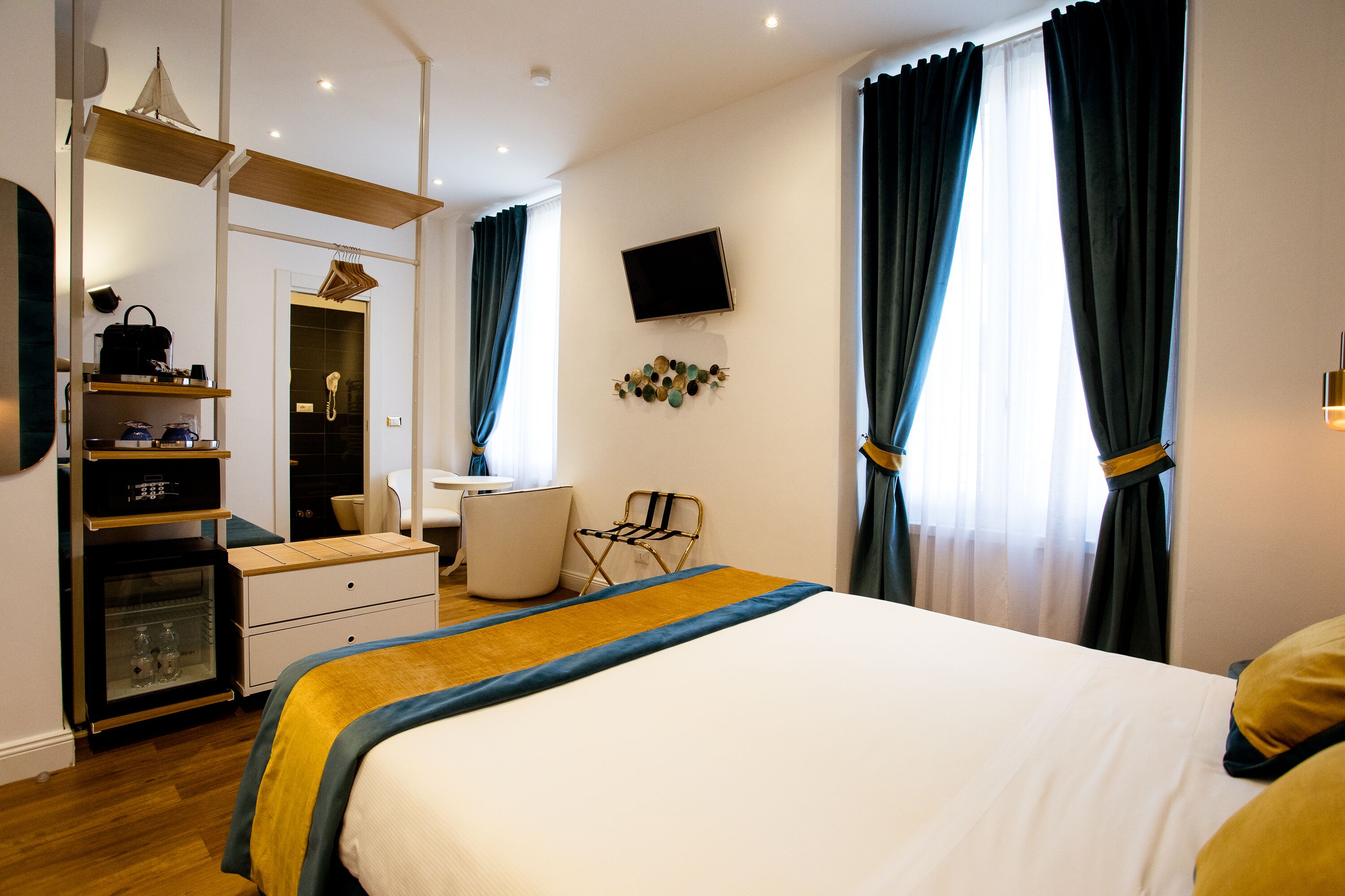 A hotel room with a bed, a desk, a chair, a wardrobe, and a TV on the wall.