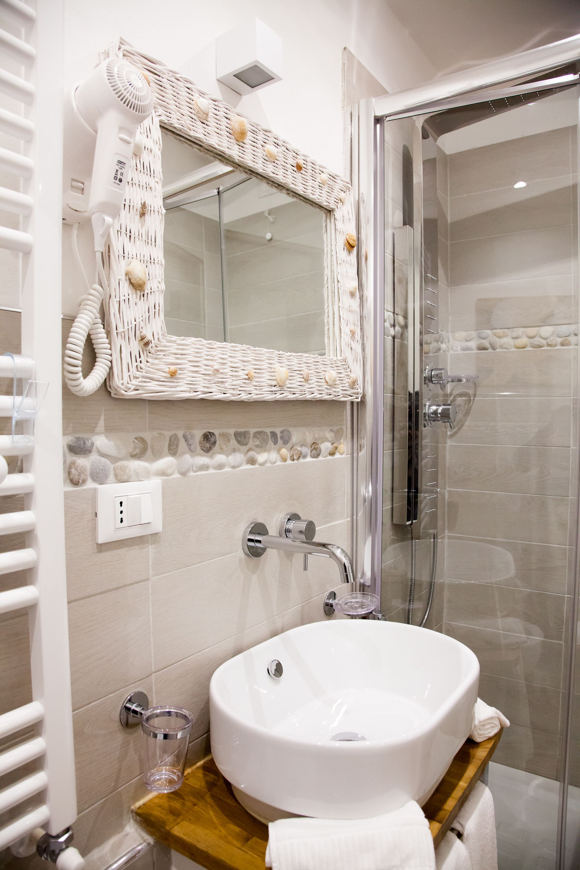 A bathroom with a white sink, a glass shower enclosure, and a wicker mirror.